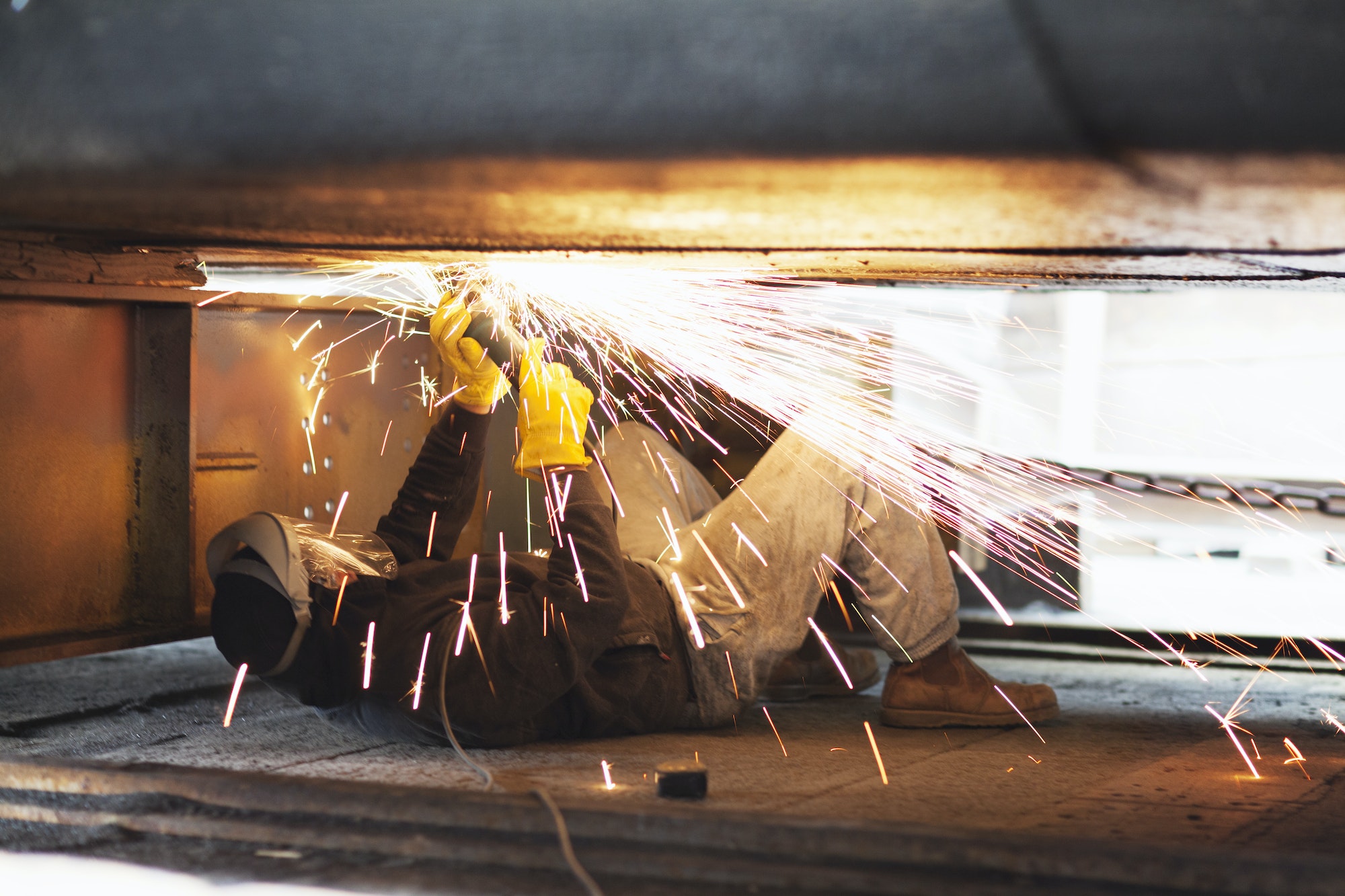 Welder welding beneath boat in shipyard workshop